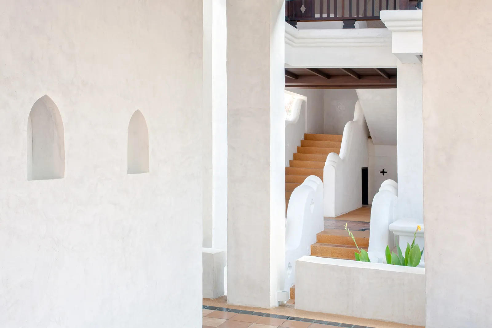White plastered corridor with pointed-arch niches and terracotta staircase