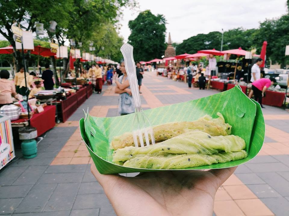 Pandan leaf crepes served in a banana-leaf boat at the Tha Nam Rap Sadet market, with the market promenade visible behind