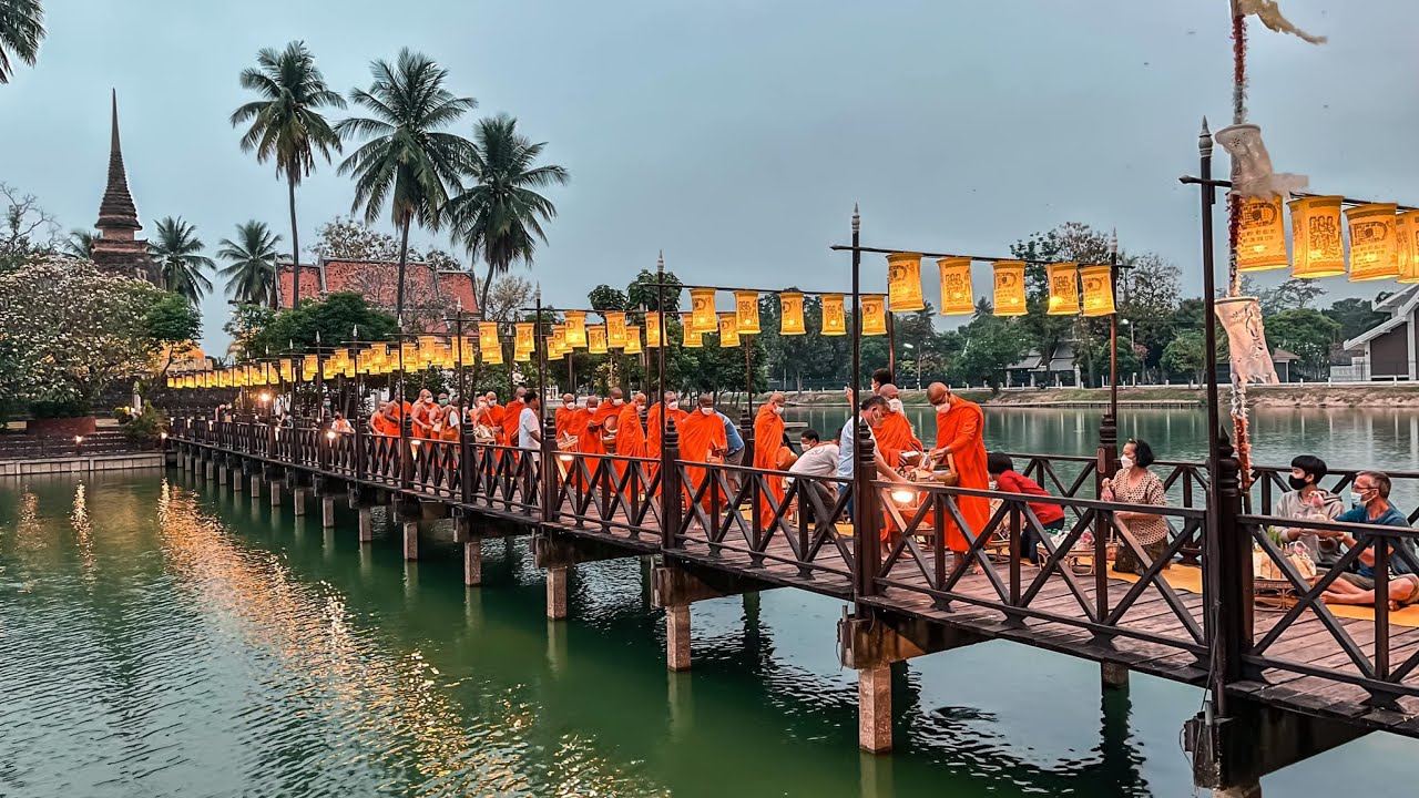 Wooden bridge leading to Wat Traphang Thong reflected in a still lotus pond at dawn
