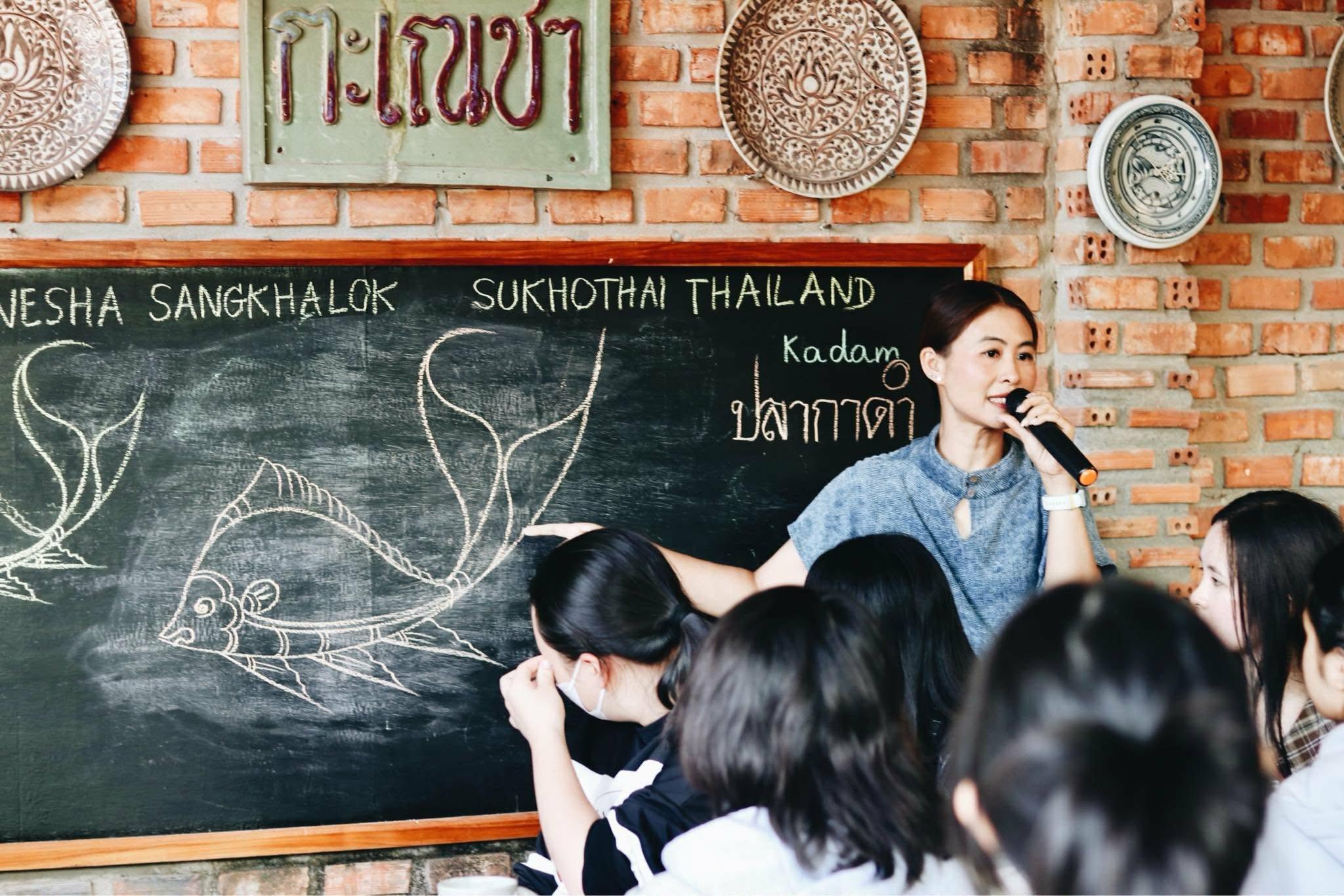 Workshop instructor teaching the traditional Sangkhalok kadam fish motif to participants at Nesha Sangkhalok studio in Sukhothai