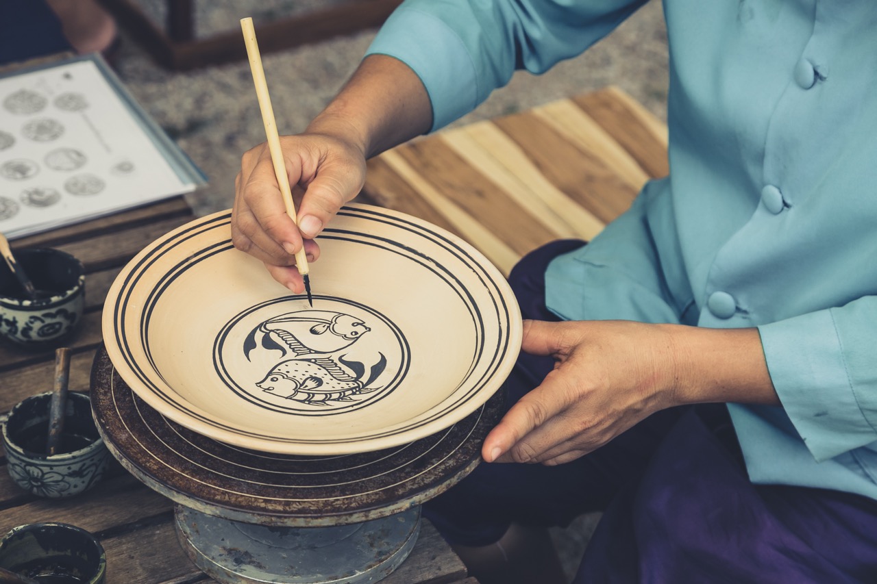 Artisan's hand painting the traditional kadam fish motif on unglazed Sangkhalok pottery