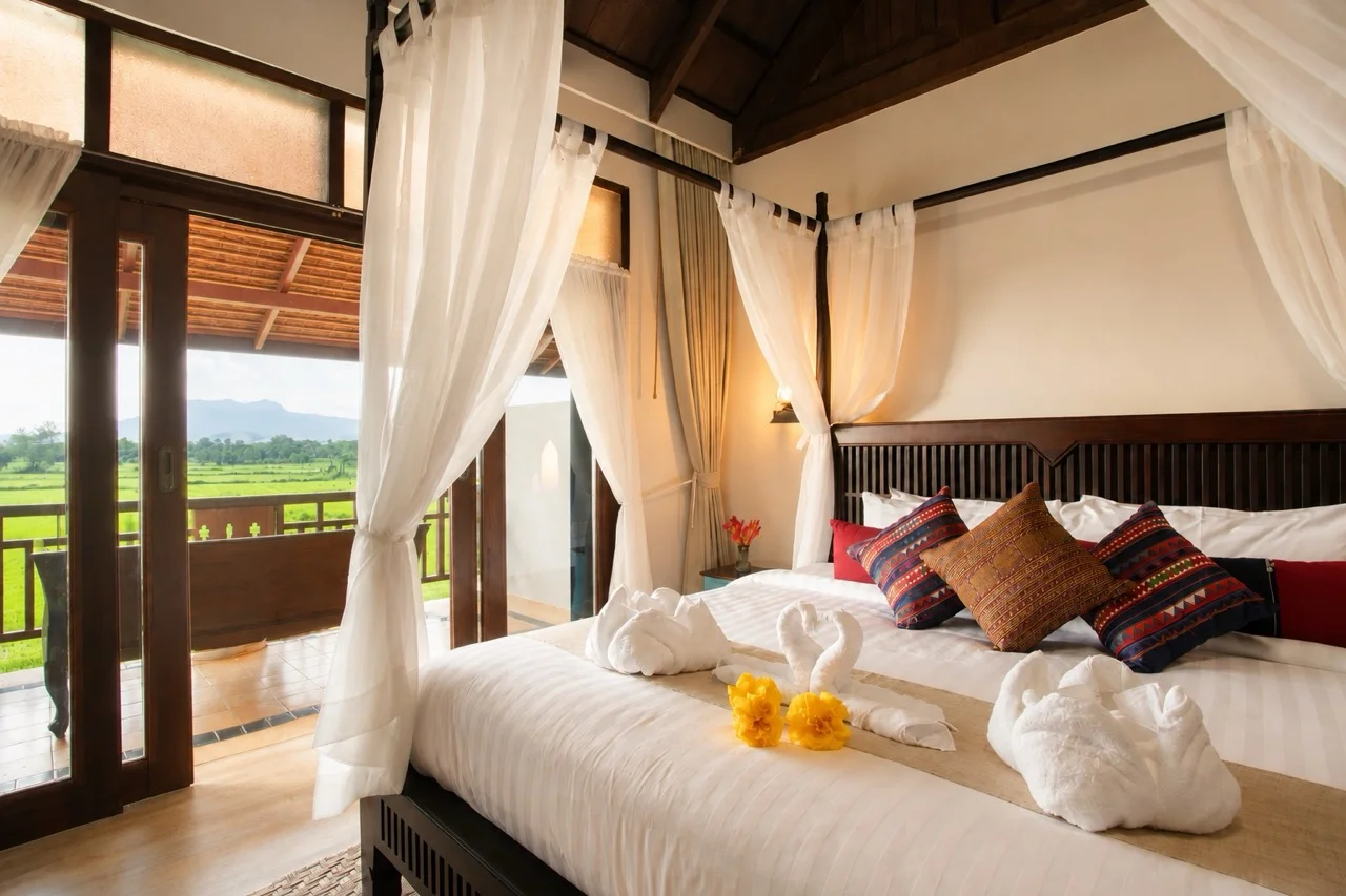 Deluxe Room — four-poster bed with open balcony doors and mountain view at golden hour